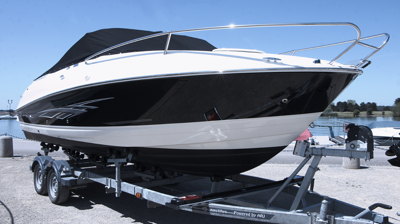 White and black motorboat on a trailer in a parking lot under bright sunlight