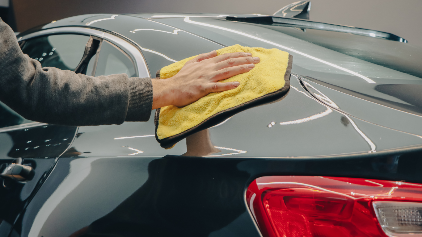 Hand polishing a dark car with a yellow cloth in a garage