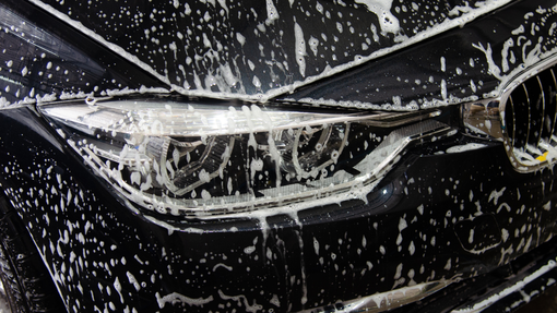 Close-up of a black car front covered in white foam during a car wash