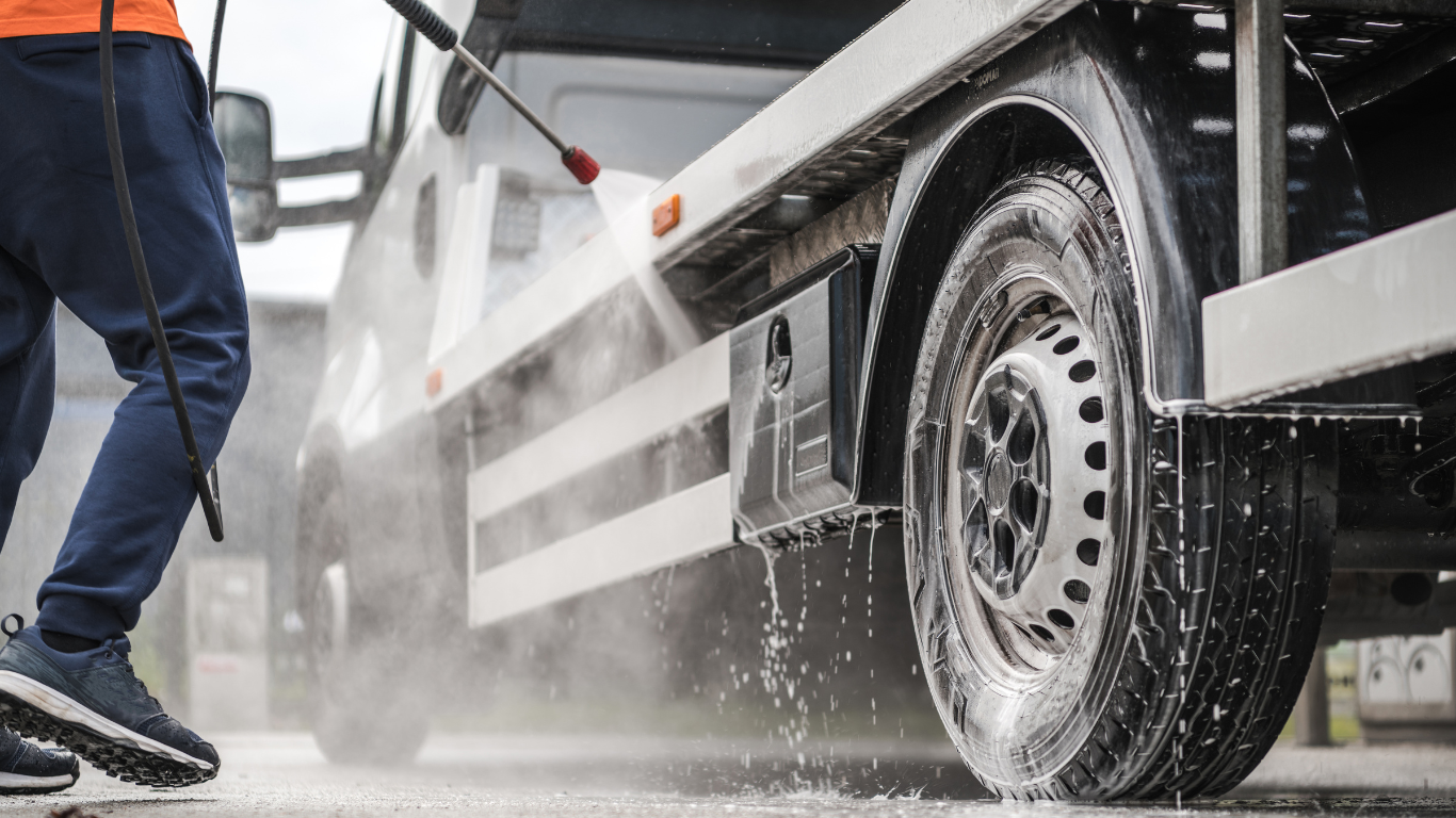Worker pressure-washing a truck’s wheel and side panel outdoors