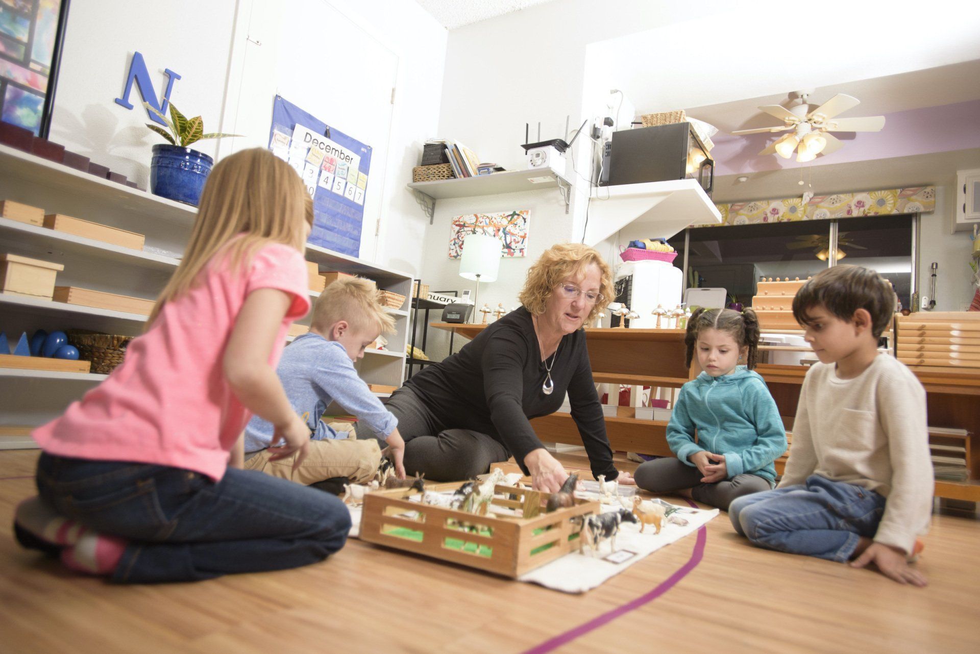 Children sitting on colorful mats in a bright classroom, facing a seated teacher during circle time