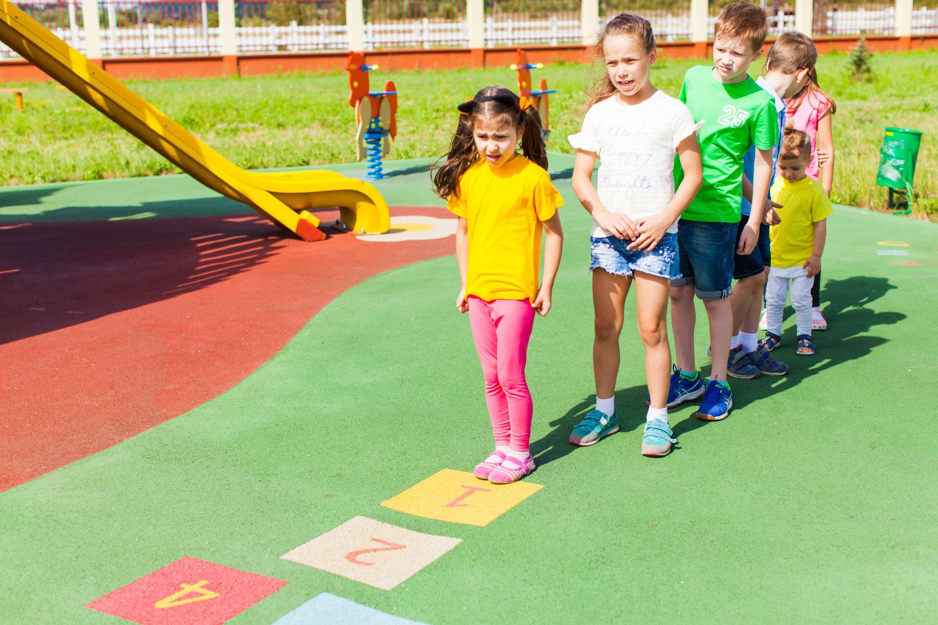 Children standing in line on a colorful playground, waiting on numbered spots.