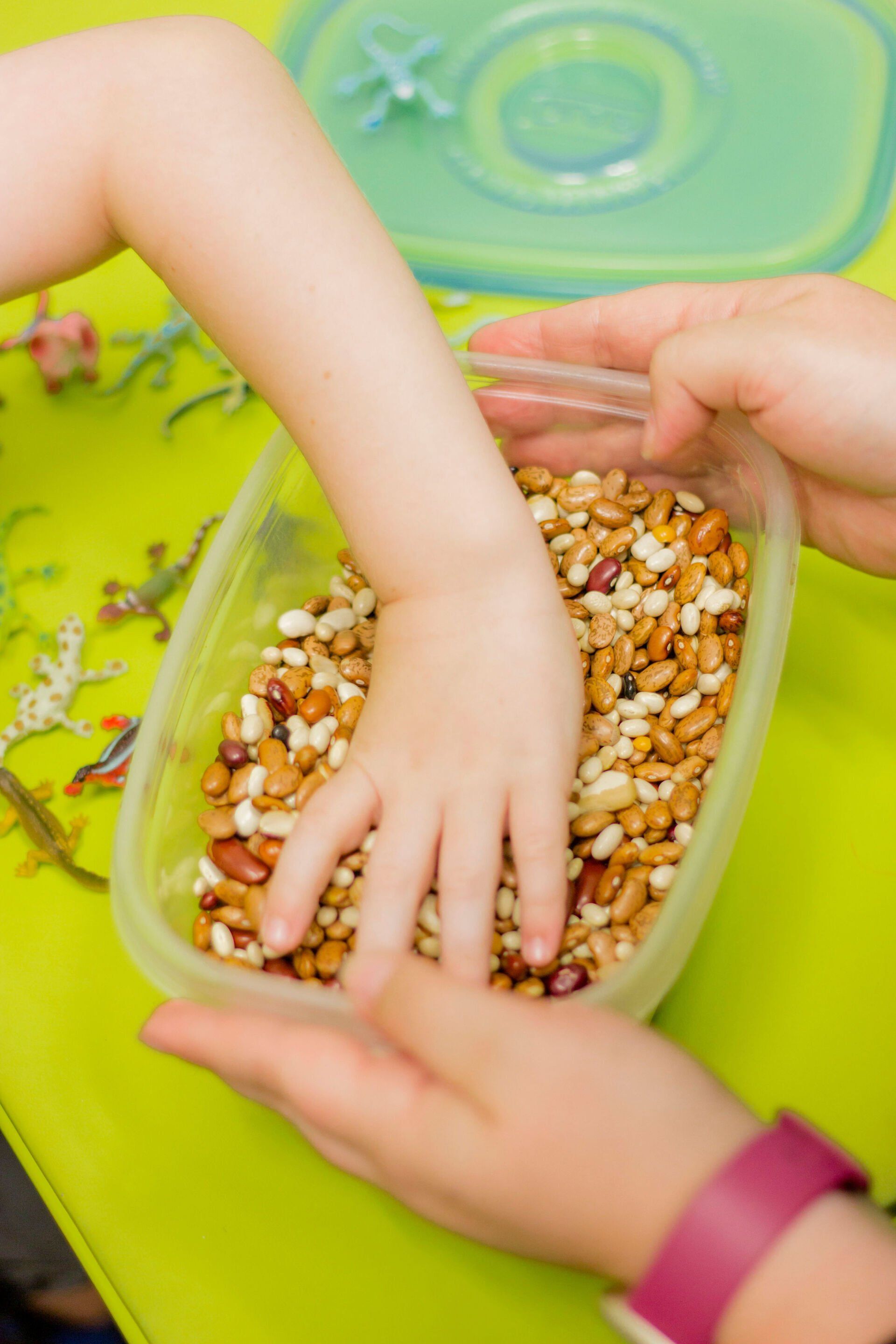 Hands sorting mixed beads in a clear container on a green table