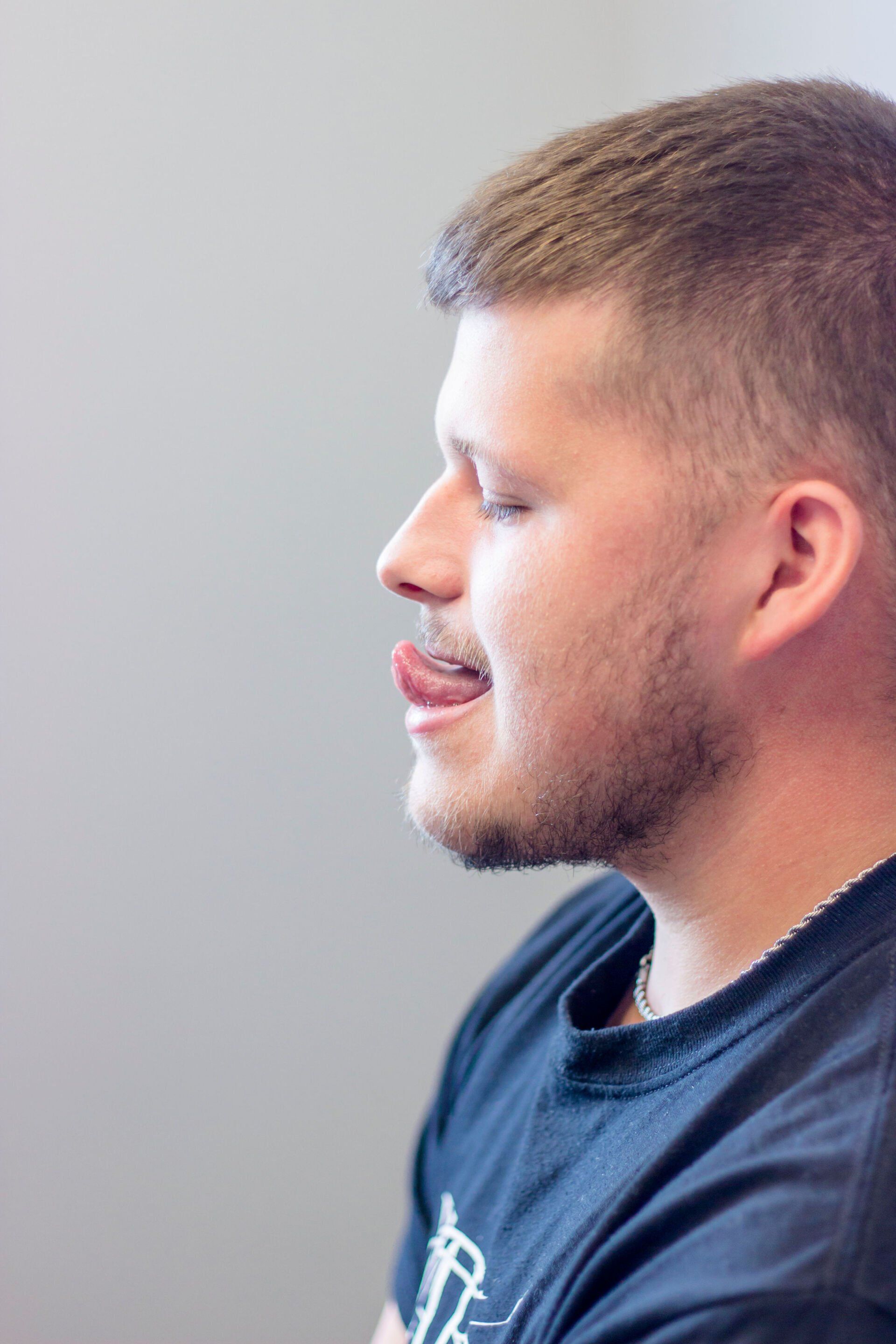 Side profile of a man with short hair and beard, wearing a navy shirt, against a light background