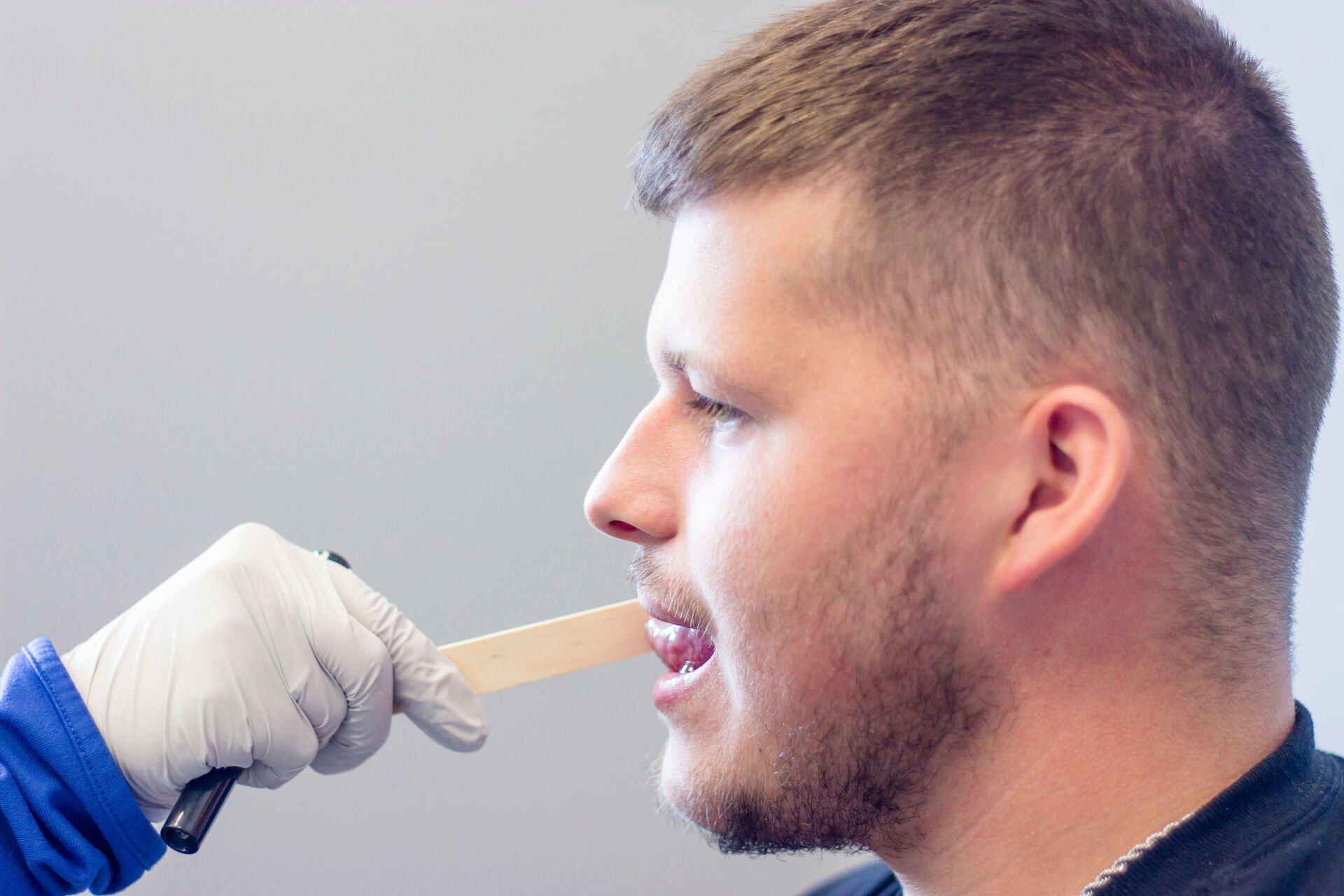 Healthcare worker swabbing a man's throat with a wooden tongue depressor and gloved hand