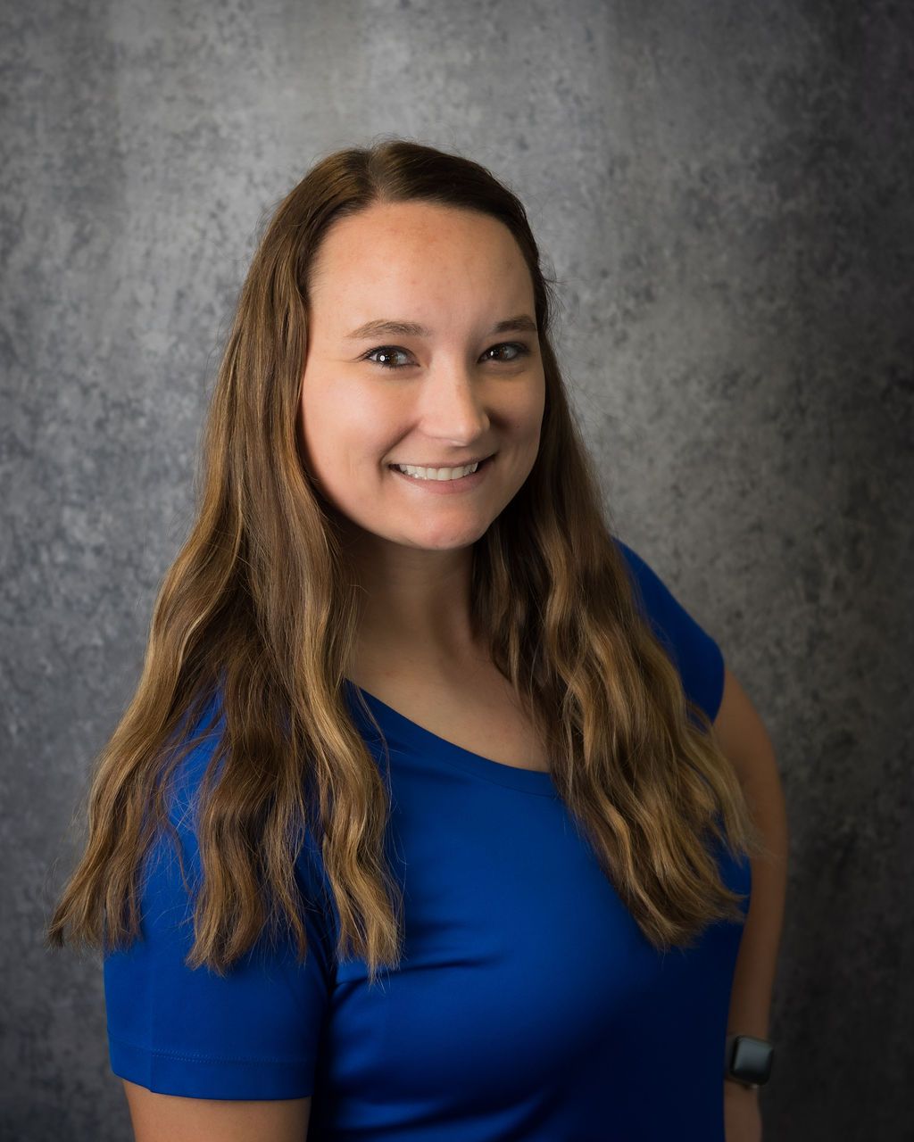 Smiling woman in a blue shirt standing against a gray textured backdrop