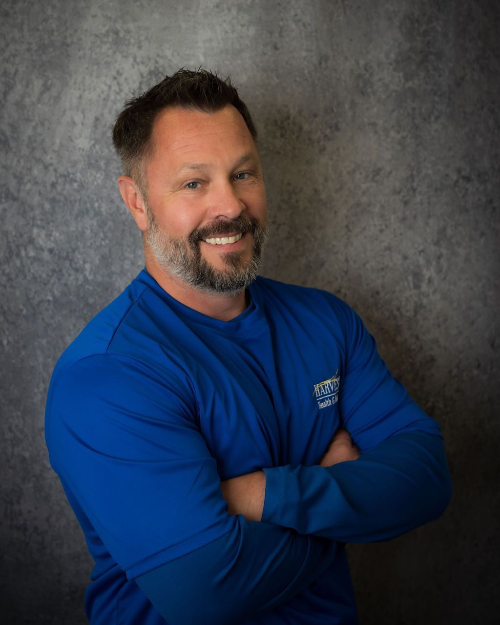 Smiling man in a blue shirt with arms crossed against a gray studio backdrop