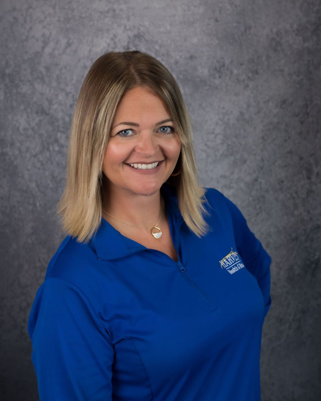 Smiling woman in a blue polo shirt against a gray studio backdrop