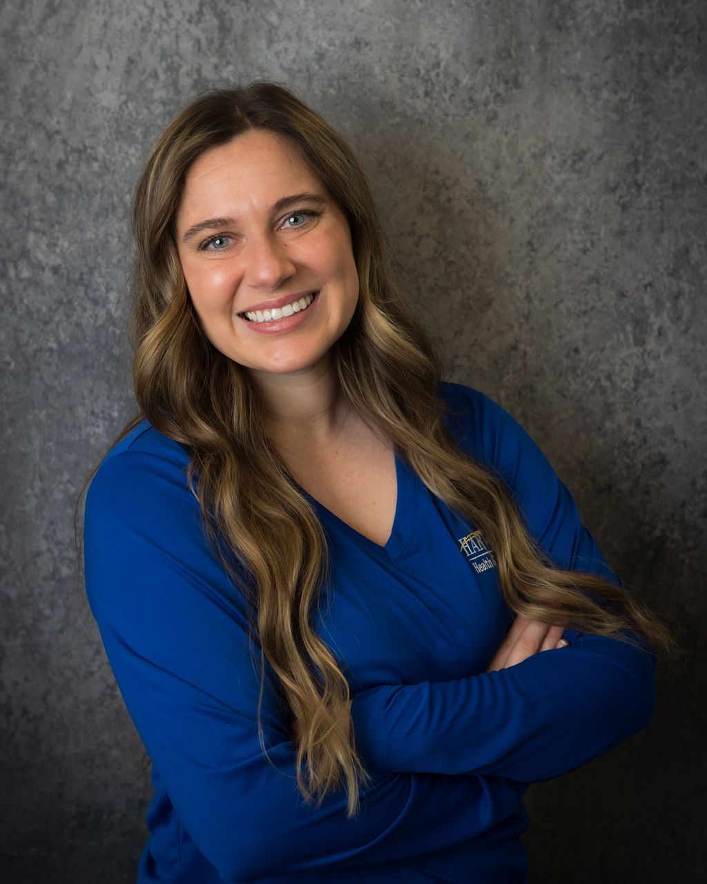 Smiling person in a blue top with arms crossed against a gray studio backdrop