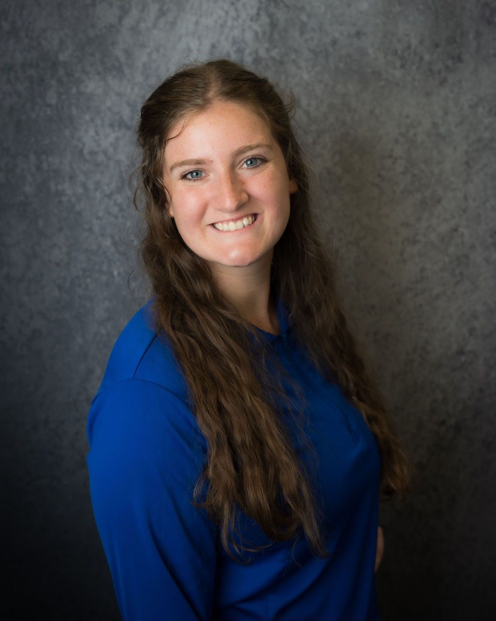 Smiling person in a blue top posed against a gray studio backdrop.