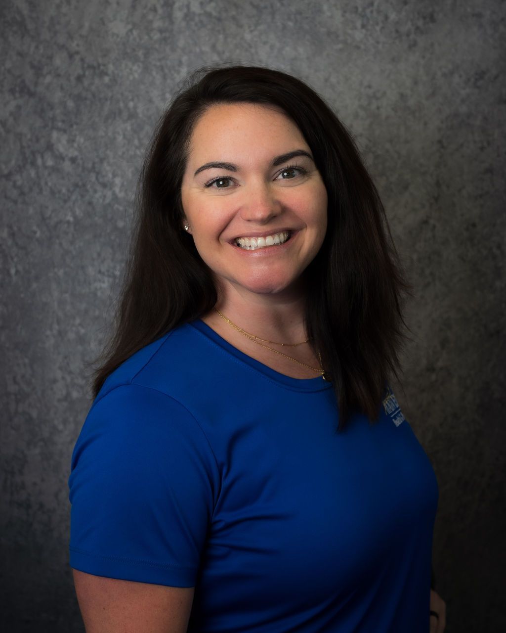 Smiling person in a blue shirt against a gray studio backdrop