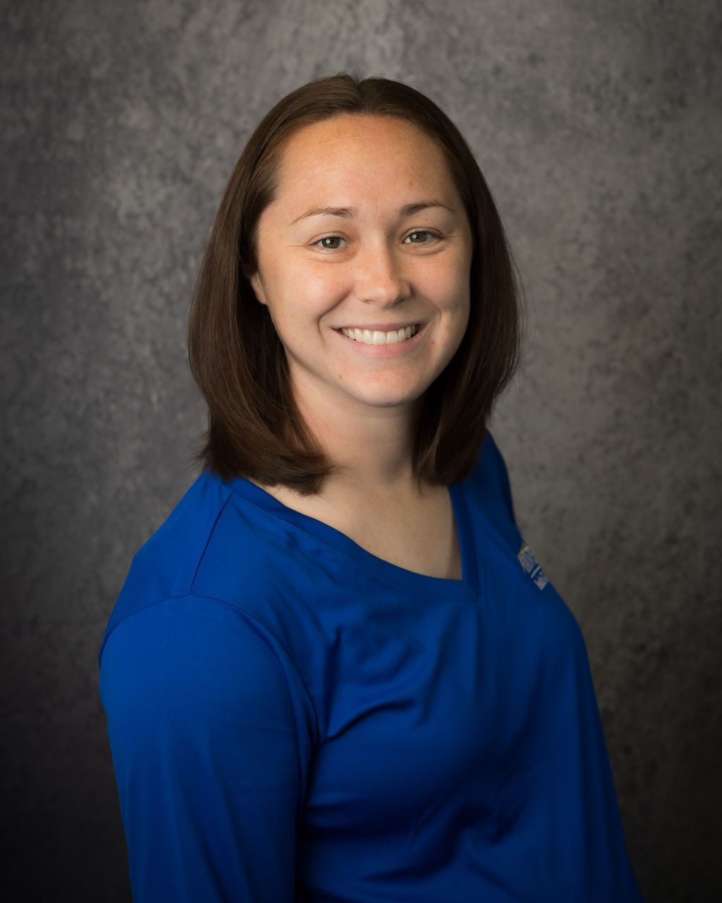 Smiling woman in a blue top against a gray studio background