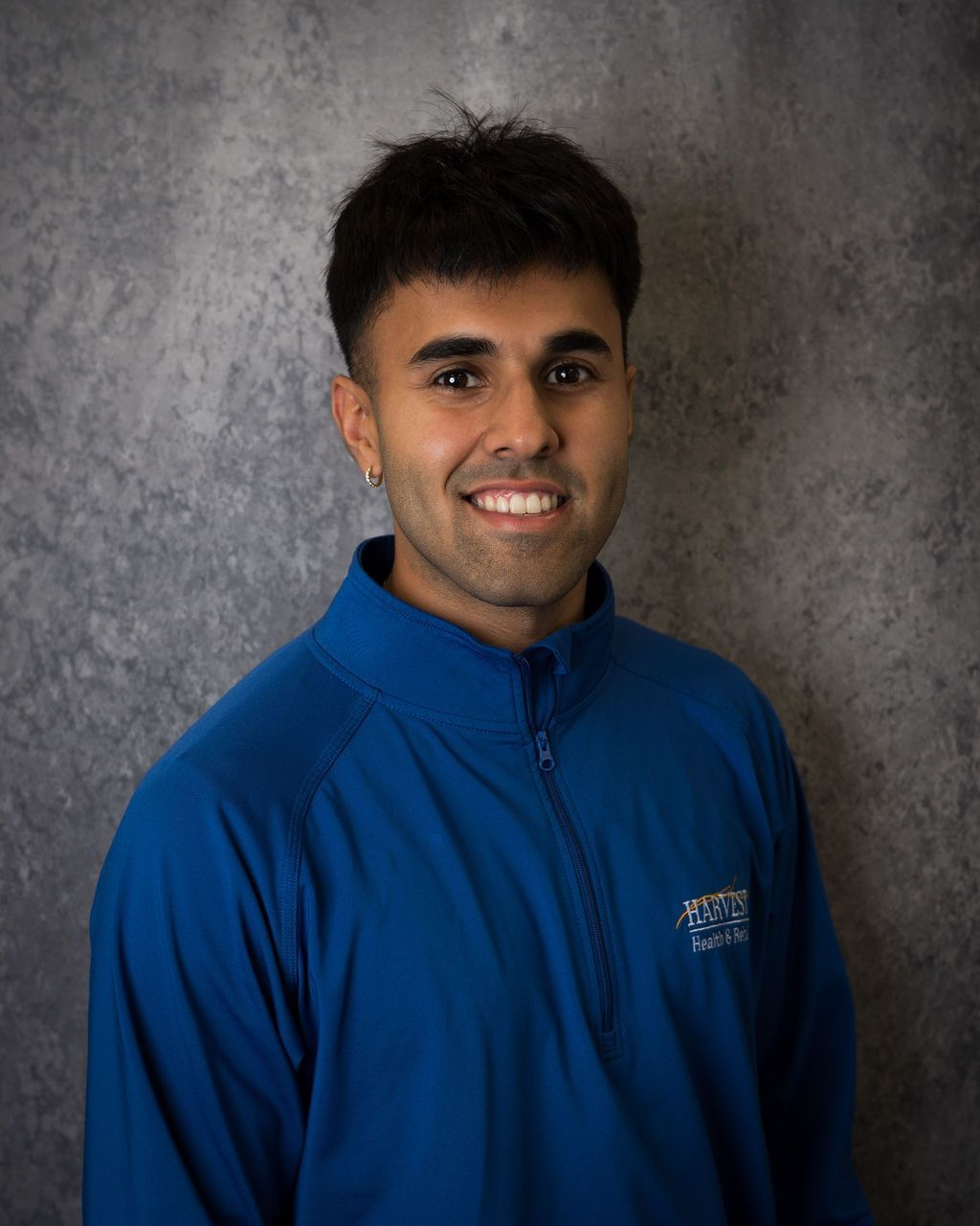 Person in a blue zip-up jacket smiling against a gray backdrop.