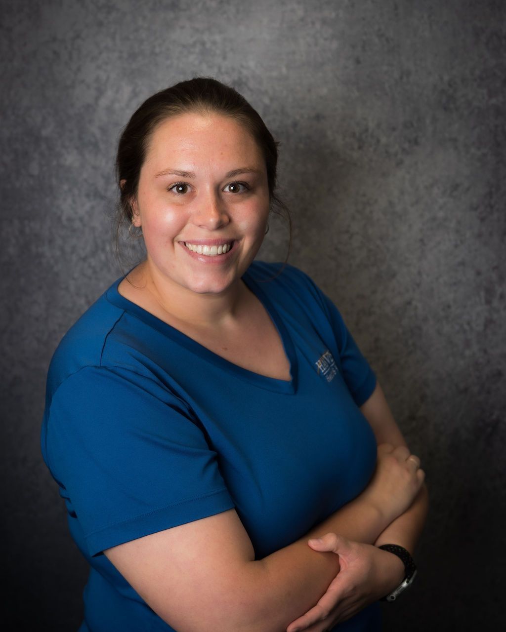 Smiling person in a blue shirt posing against a gray backdrop.