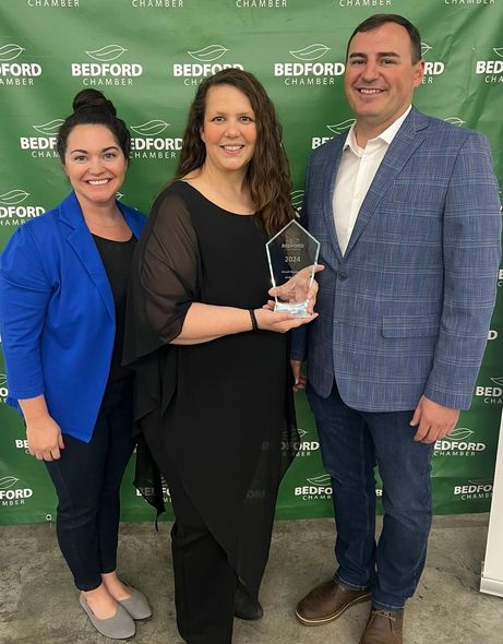 Three people posing with an award in front of a Bedford backdrop.