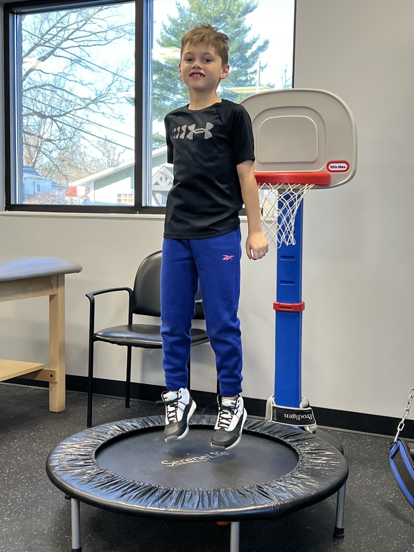 Child jumping on a trampoline indoors beside a window and basketball hoop