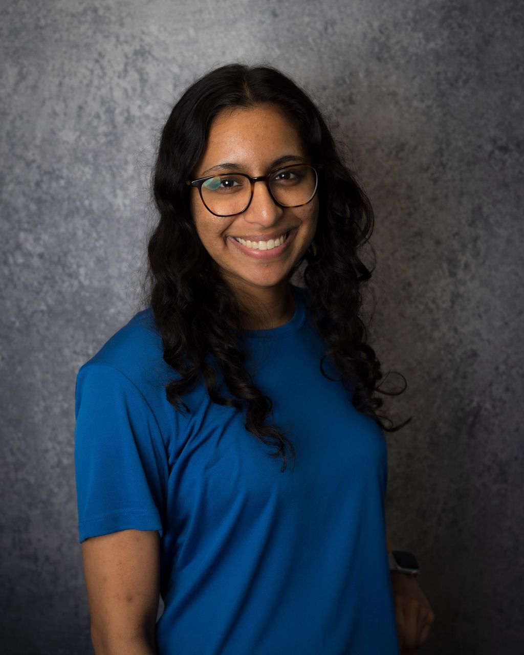 Smiling person with glasses in a blue shirt against a gray backdrop