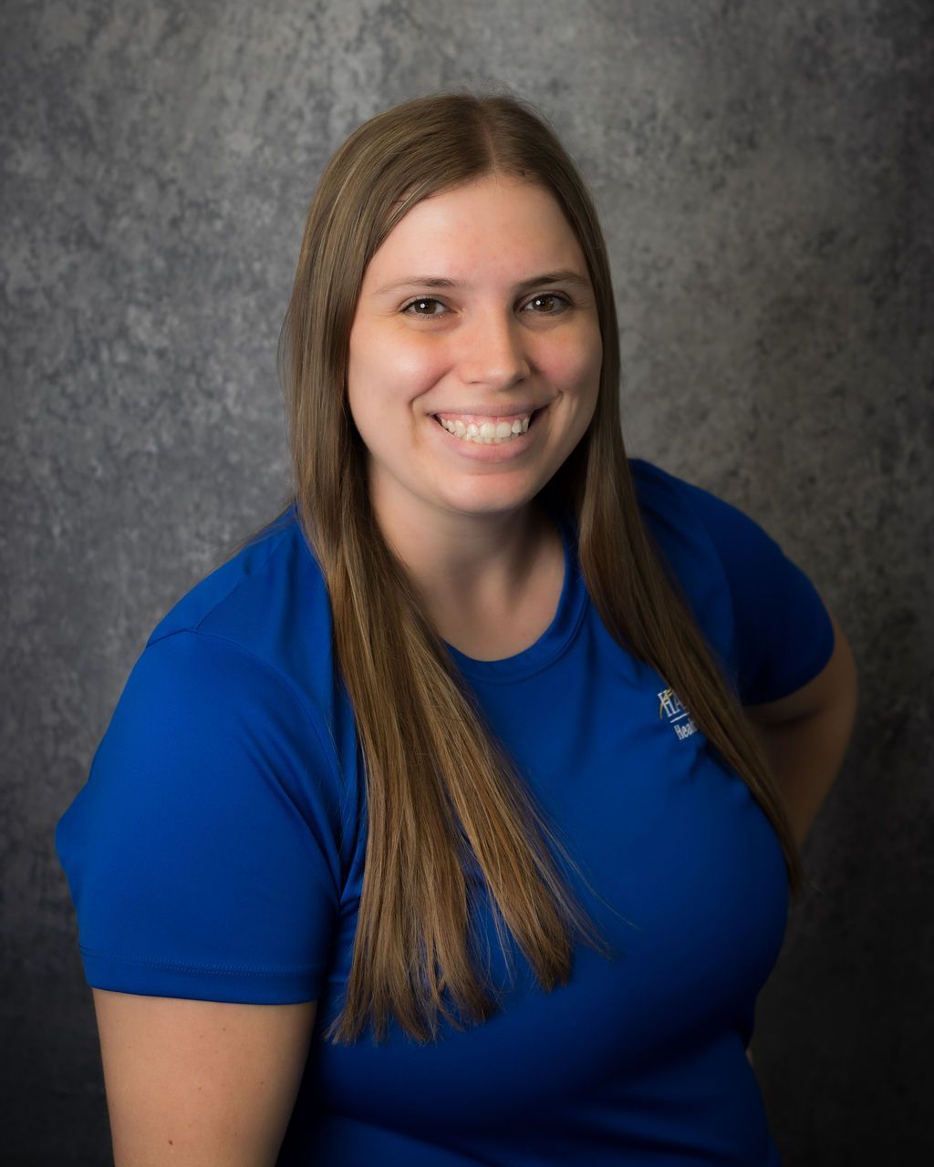 Smiling person in a blue shirt posing against a gray studio backdrop