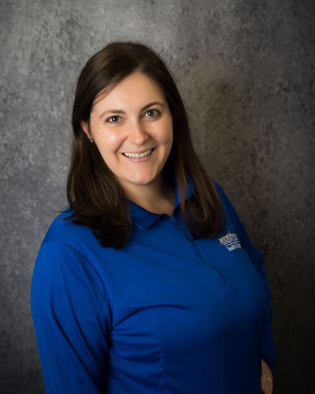 Woman in a blue polo shirt smiling against a gray studio backdrop