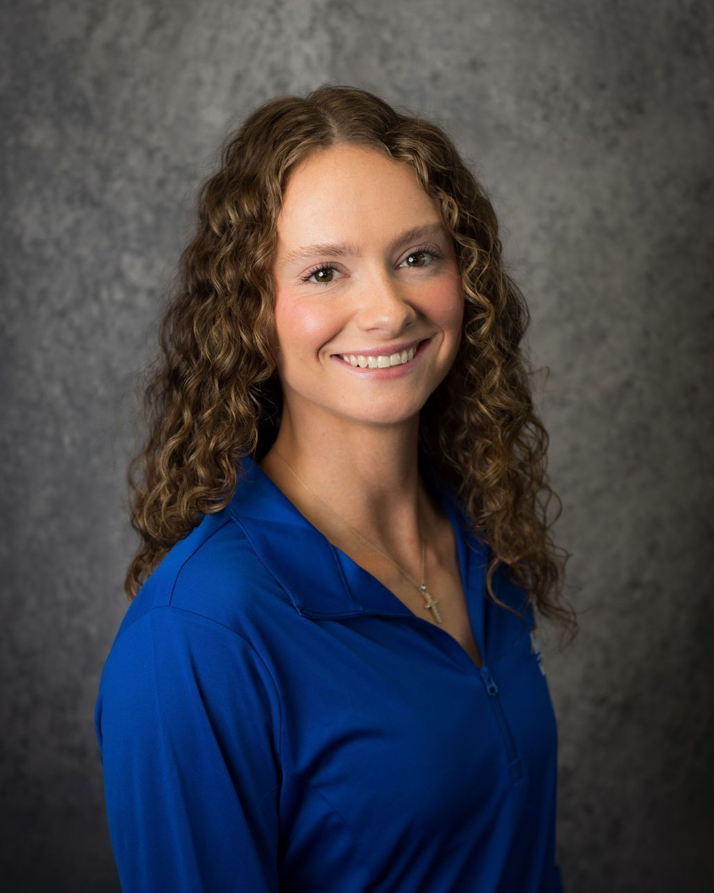 Smiling woman in a blue blouse against a gray studio backdrop