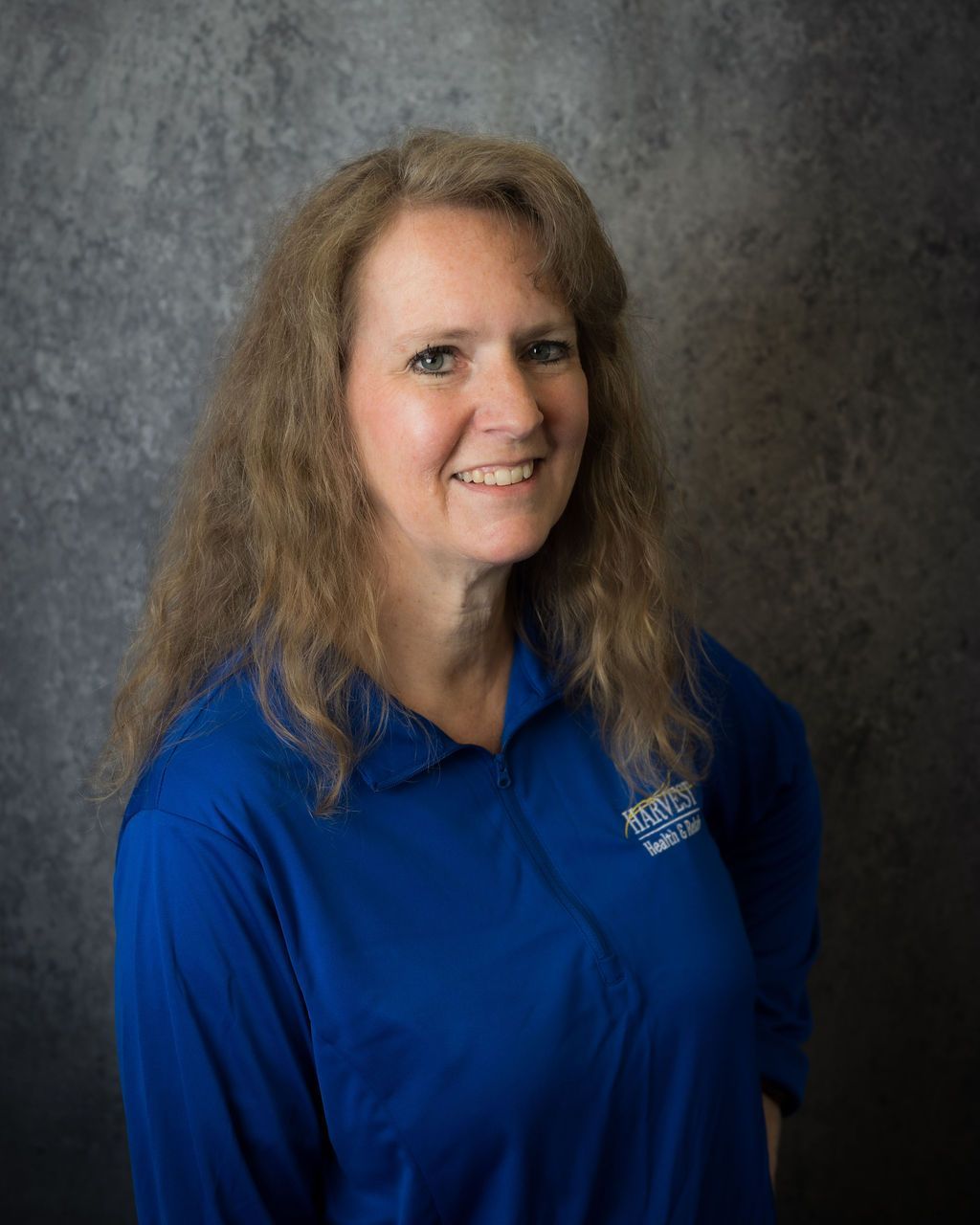Woman in a blue shirt smiling against a gray studio backdrop.
