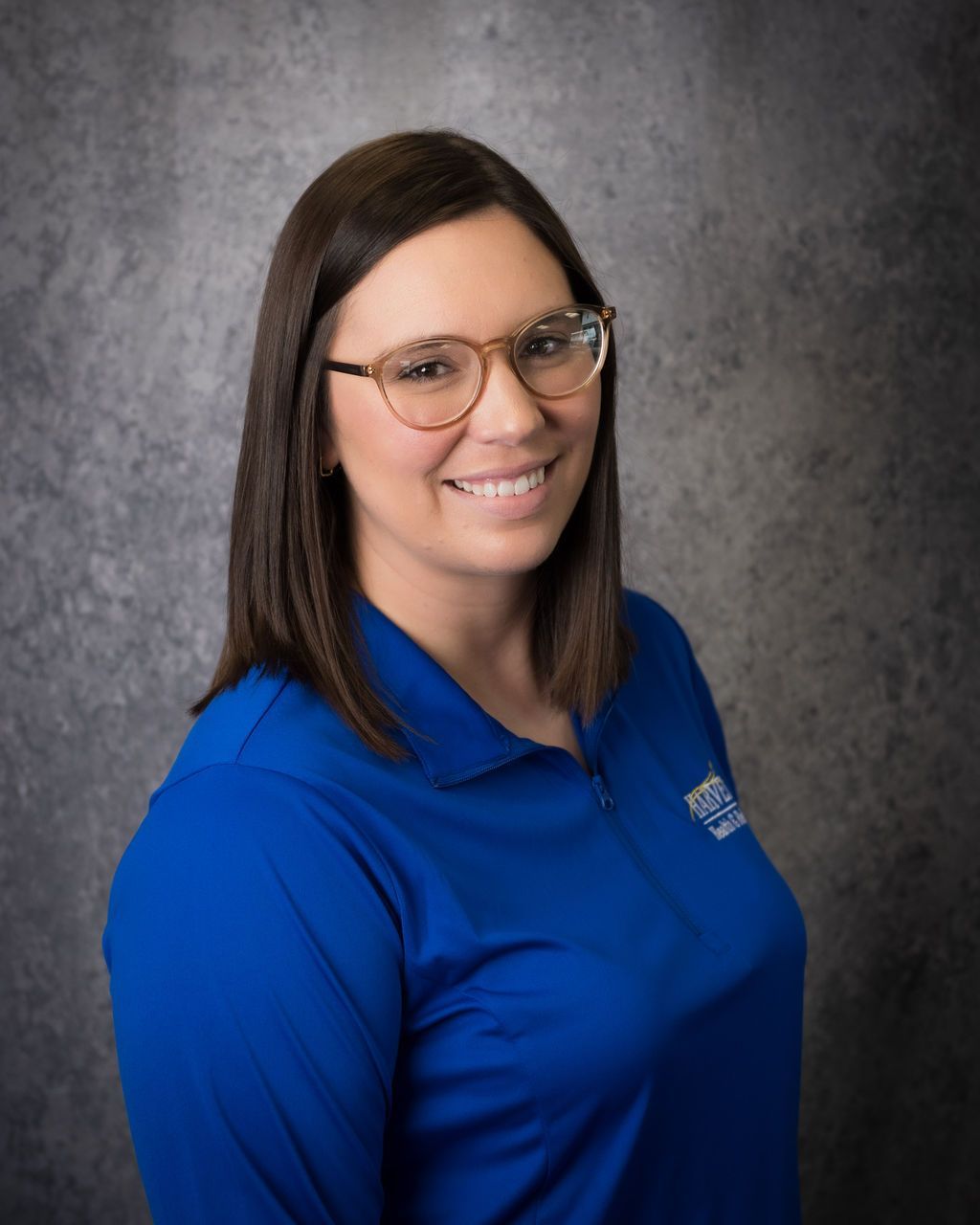 Smiling person in a blue polo shirt and glasses against a gray studio backdrop