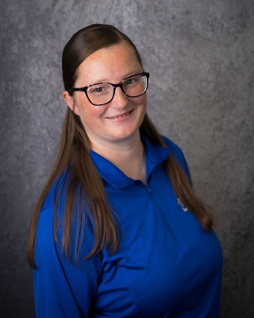Smiling person in glasses and a blue shirt against a gray backdrop