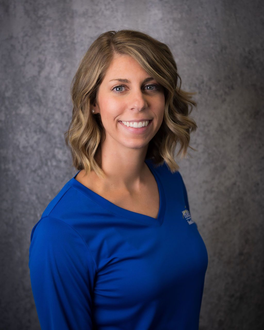 Smiling person in a blue shirt against a gray studio backdrop