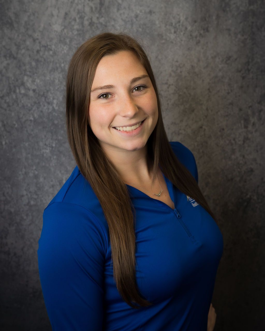Smiling person in a blue top against a gray studio backdrop