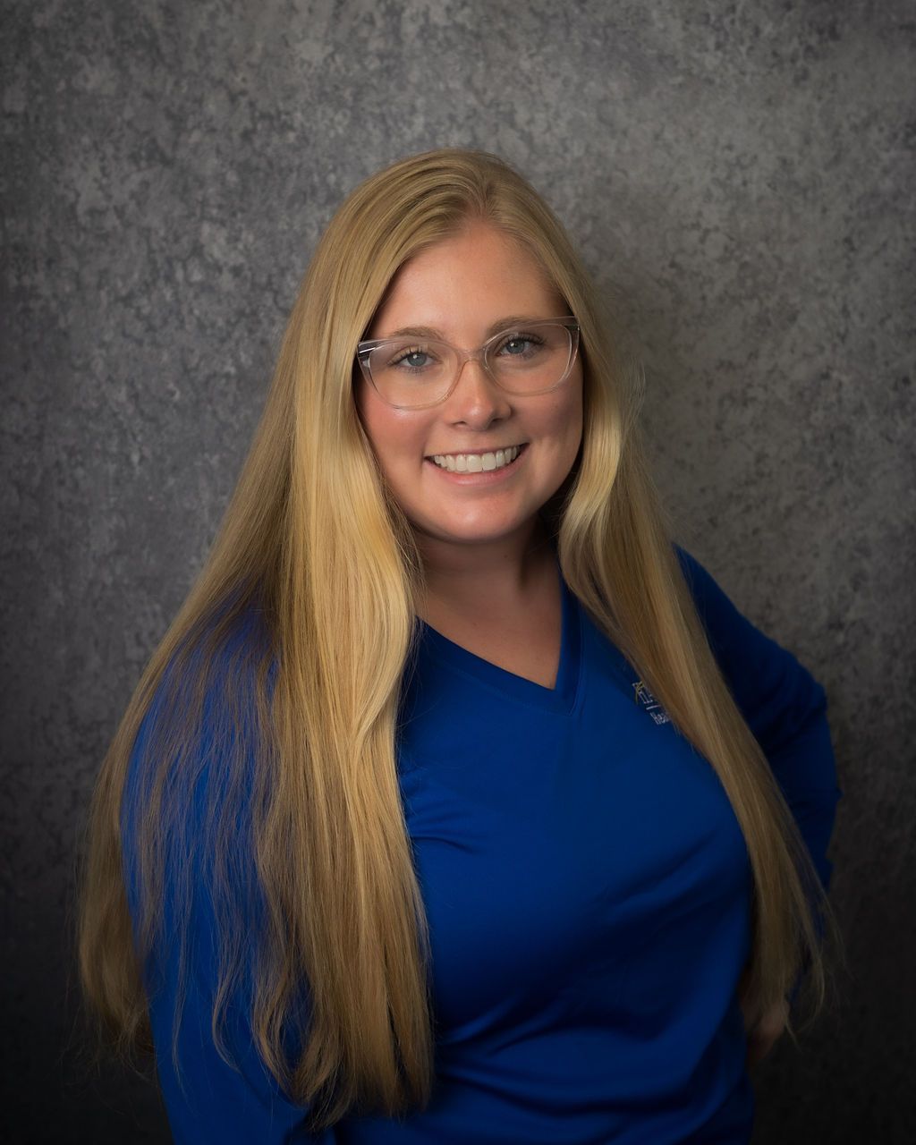 Smiling woman in glasses wearing a blue shirt against a gray backdrop