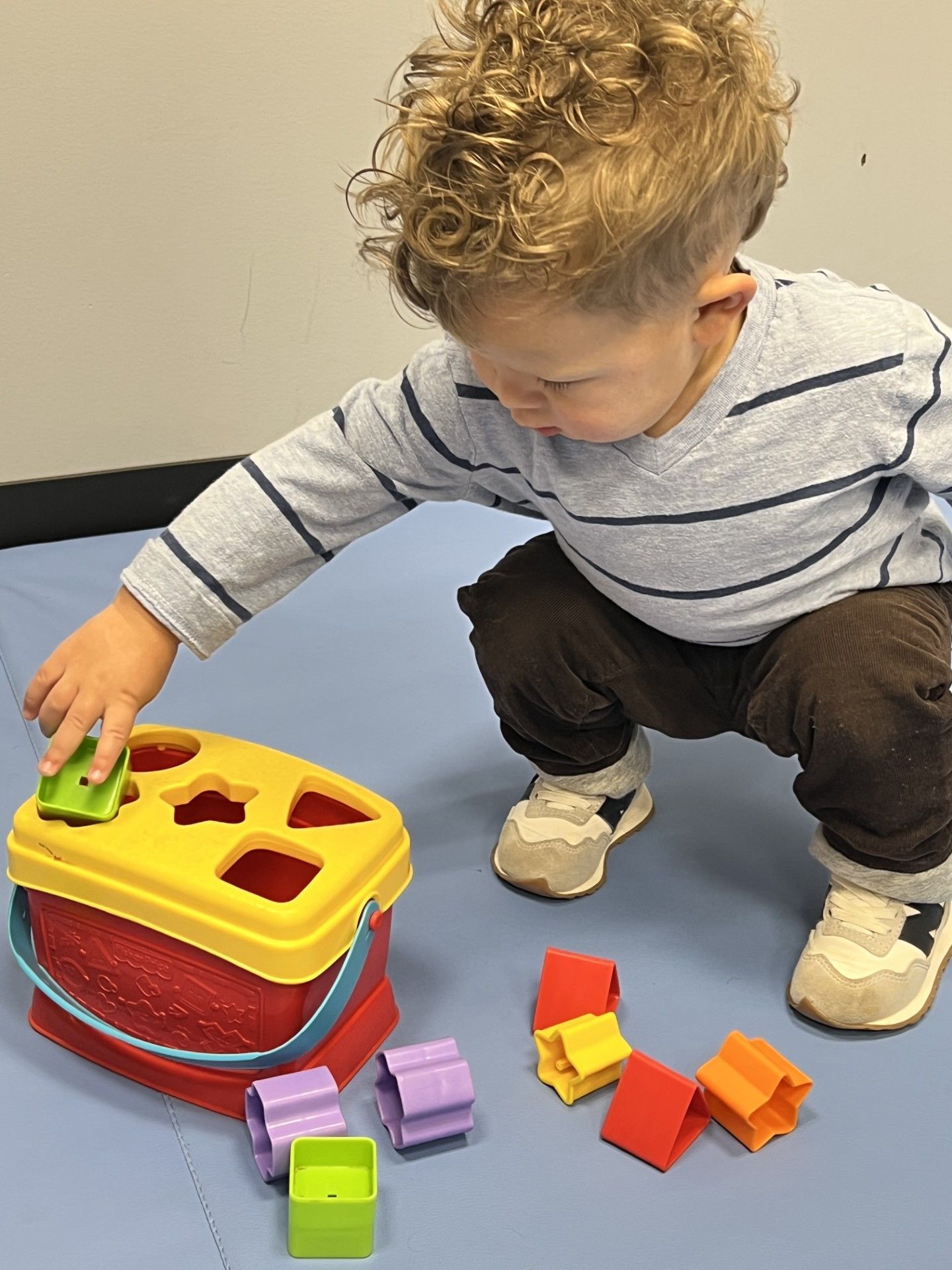 Toddler crouching and playing with colorful shape-sorting toys on a blue carpet