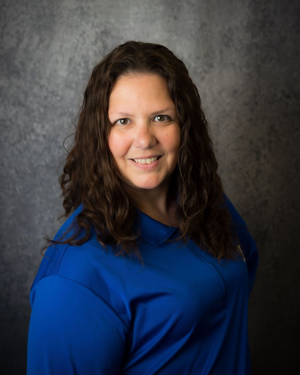 Smiling woman in a blue top against a dark gray studio backdrop