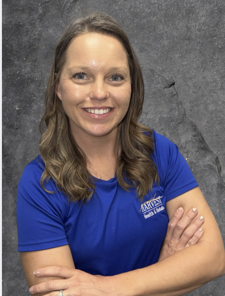 Smiling woman in a blue shirt with arms crossed against a gray backdrop