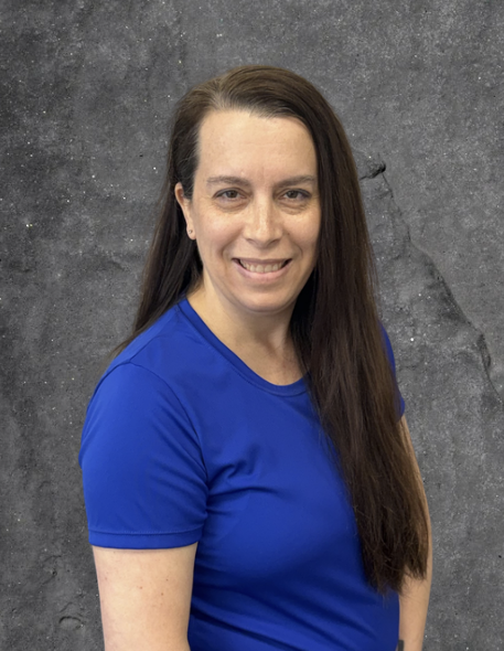 Woman in a blue shirt smiling against a gray studio backdrop