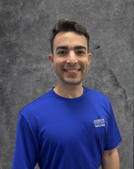 Smiling person in a royal blue T-shirt standing before a gray textured background
