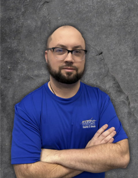 Person in a blue shirt with folded arms standing against a gray backdrop.