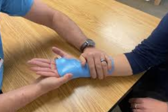 Hands applying a blue wrap to a wrist on a wooden table