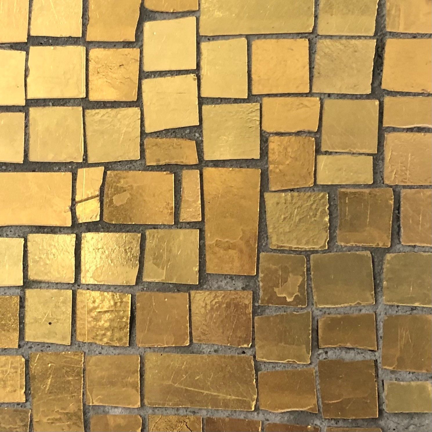 Gold mosaic tiles embedded in gray grout.
