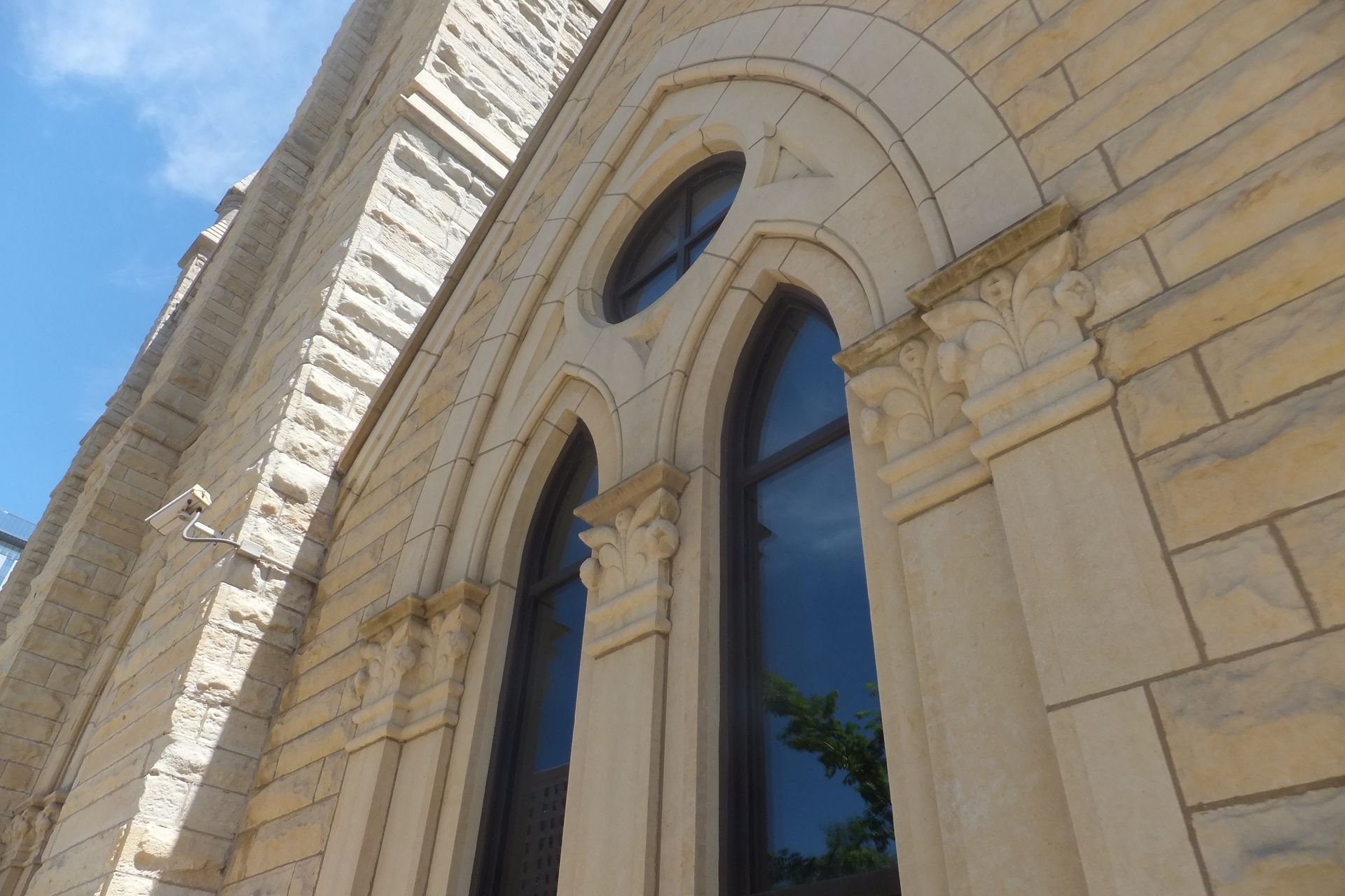 Exterior of a light-colored stone building with arched windows and a blue sky above.