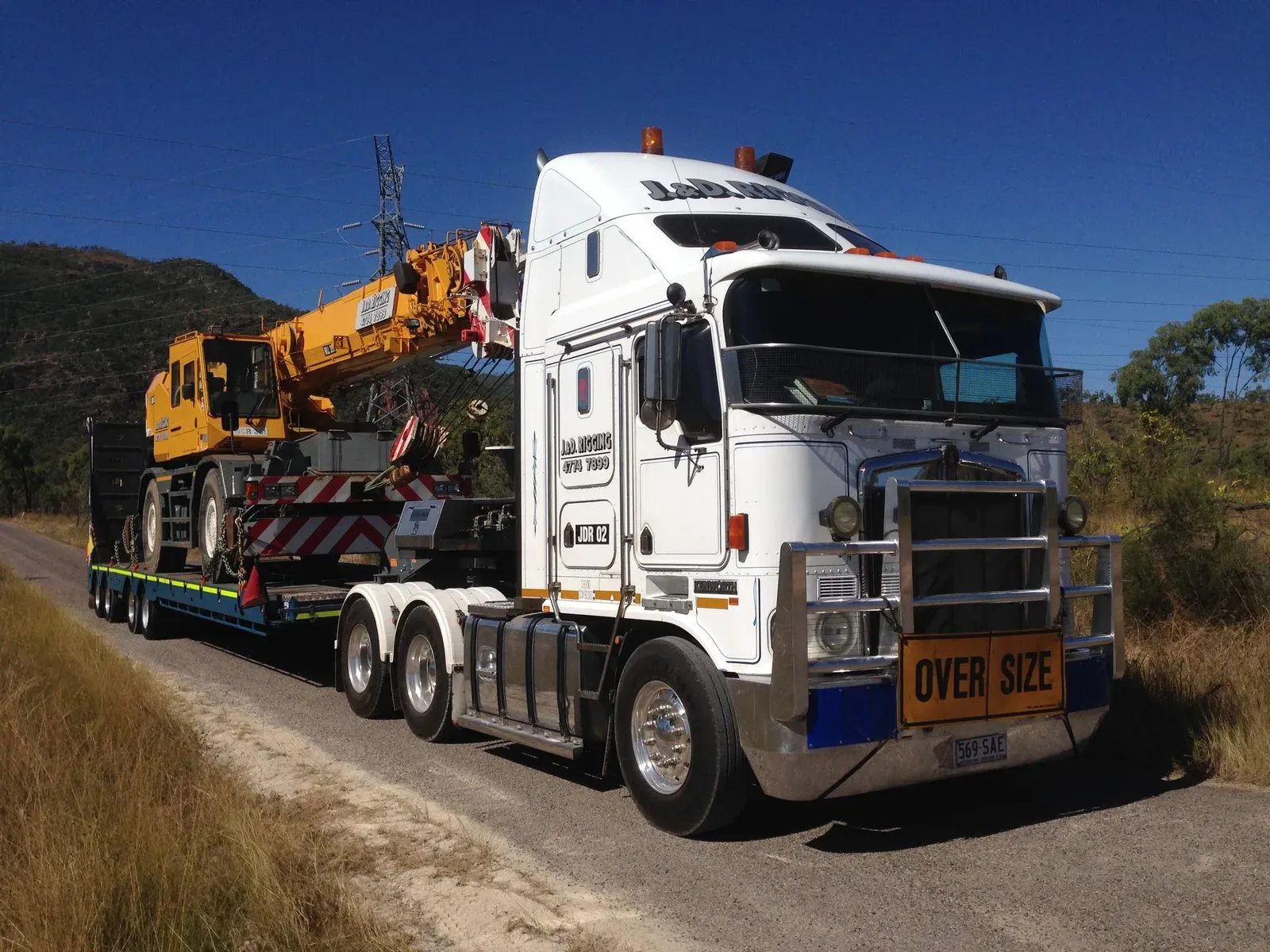 A White Semi Truck With A Yellow Sign That Says Over Size — J & D Rigging Pty Ltd In Bohle, QLD