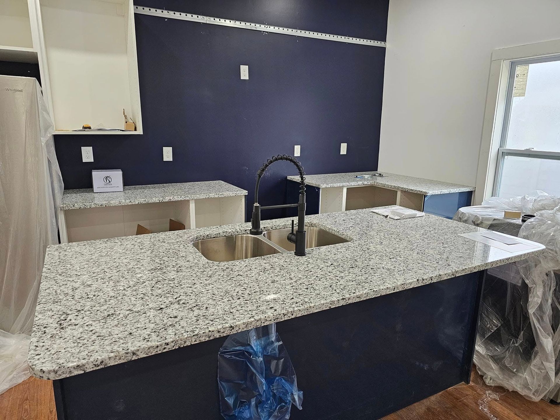 Newly constructed kitchen with a blue island and countertops, stainless steel sink.