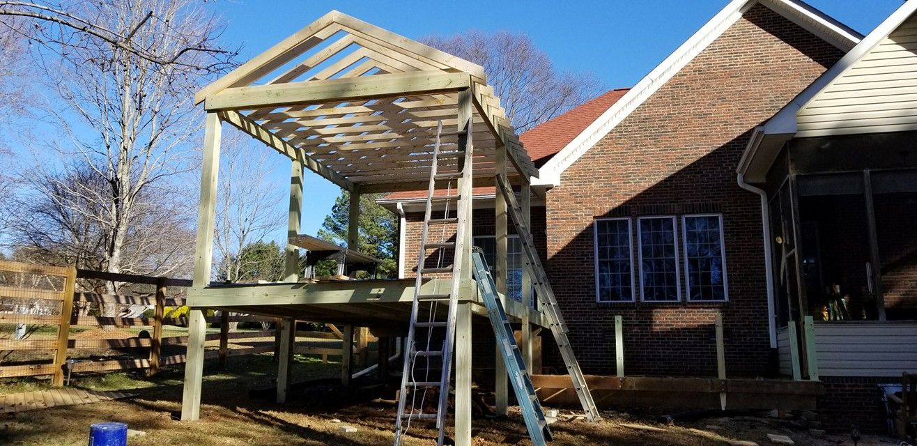 A partially constructed wooden deck and pergola attached to a brick house on a sunny day.