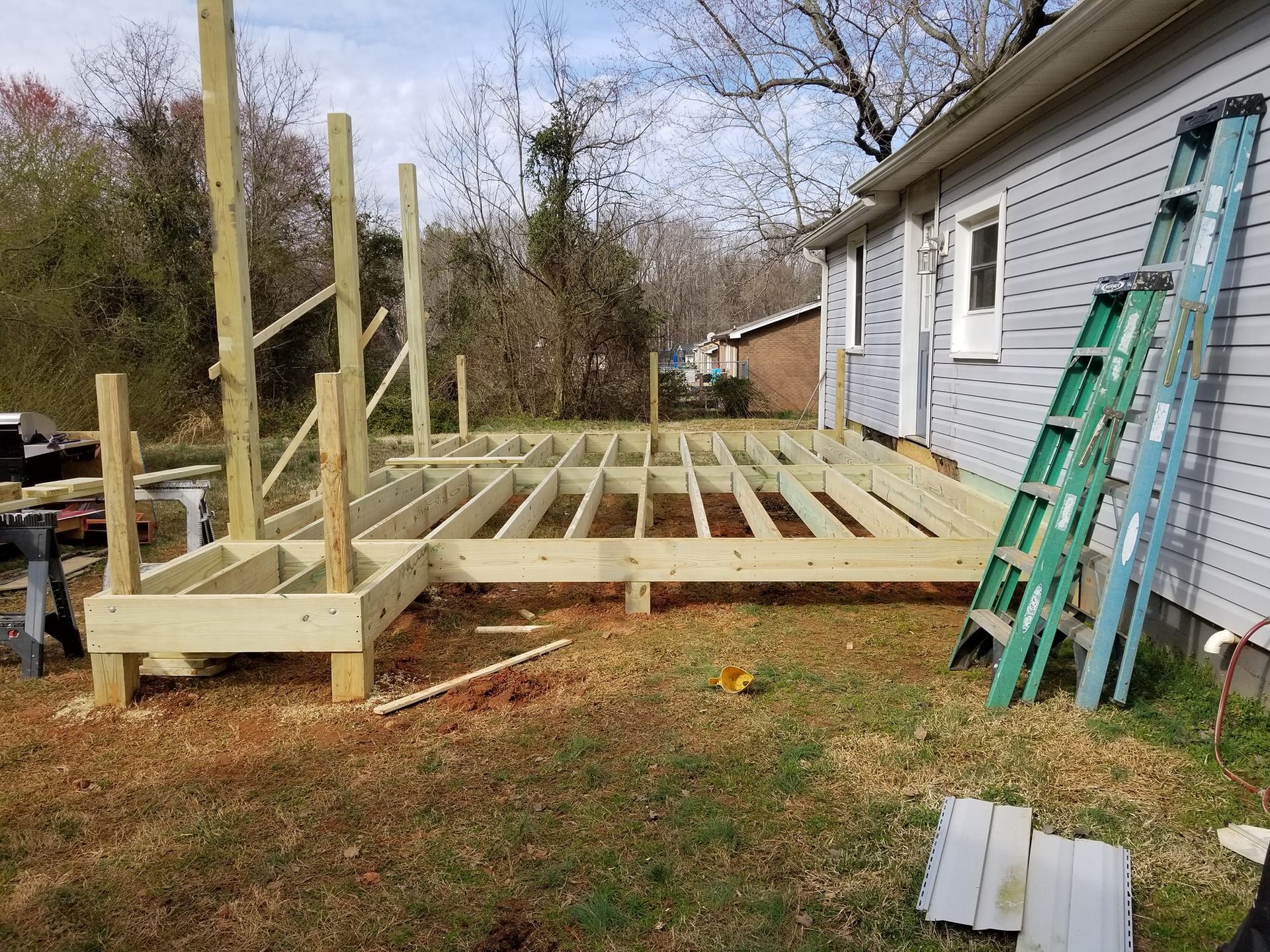 Wooden deck under construction next to a house with a green ladder leaning against the siding.