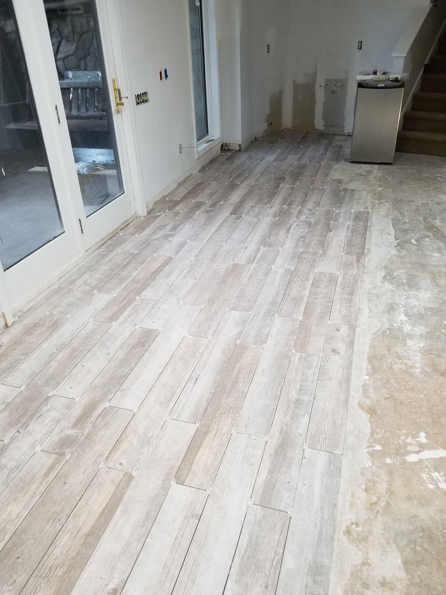 Light-colored, weathered wood-look flooring being installed in a room with white walls and a stainless steel appliance.
