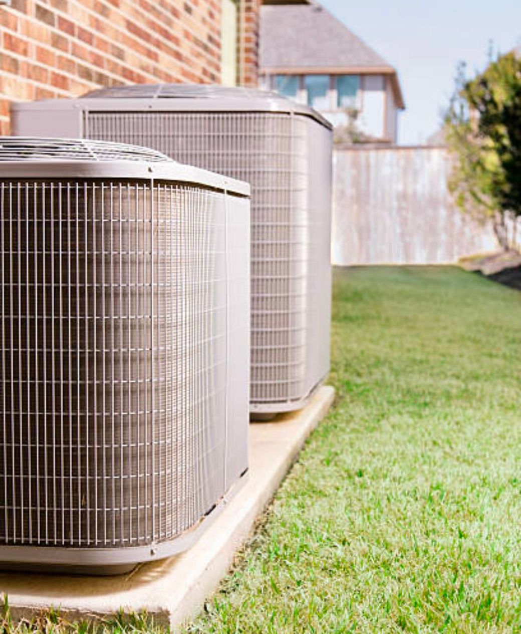 Two outdoor air conditioning units beside a house on a grassy lawn