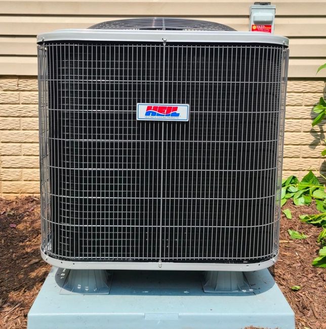 Outdoor central air conditioner unit with black grille on a concrete pad beside a house wall.