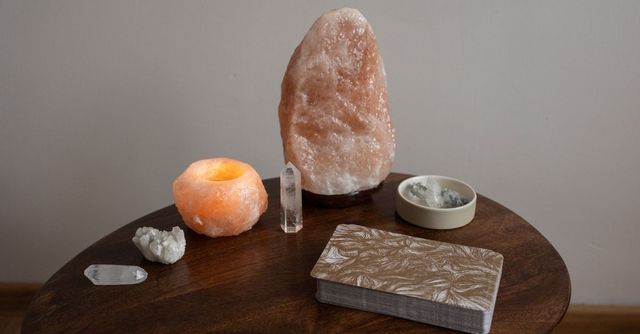 Salero y portavelas variados sobre una mesa redonda oscura, con una gran lámpara de cristal rosa y un cuenco pequeño
