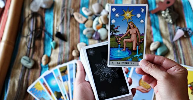 Manos sosteniendo cartas del tarot sobre una tirada de cartas coloridas en una mesa con cristales y cuentas