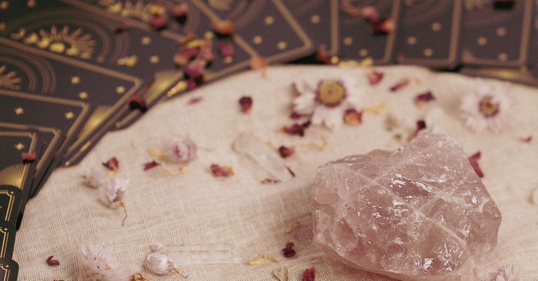 Cristal rosa sobre una superficie de tela color crema, con pétalos secos esparcidos y un fondo oscuro estampado
