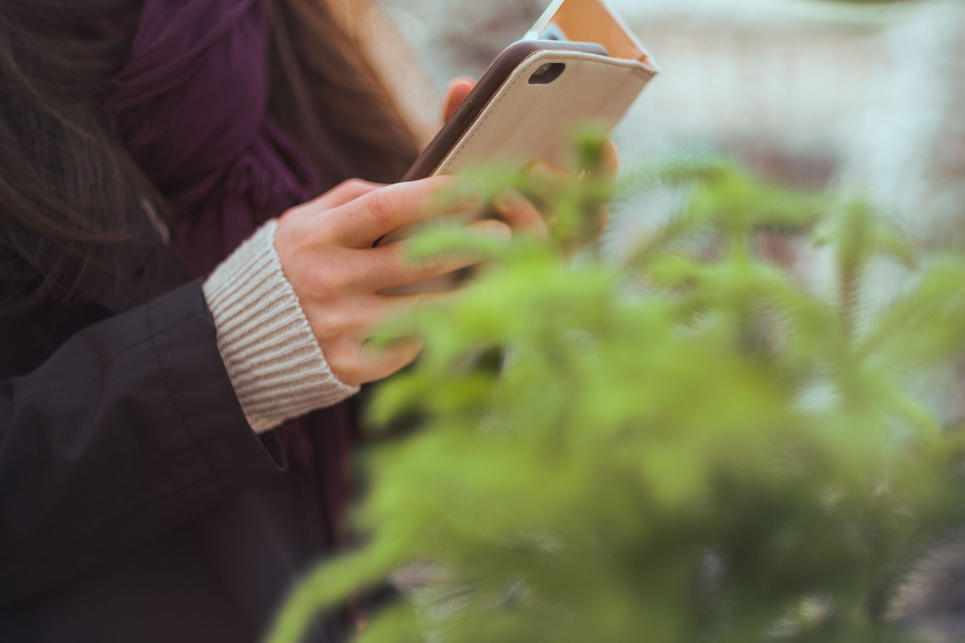 Person holding a smartphone outdoors near blurred green plants